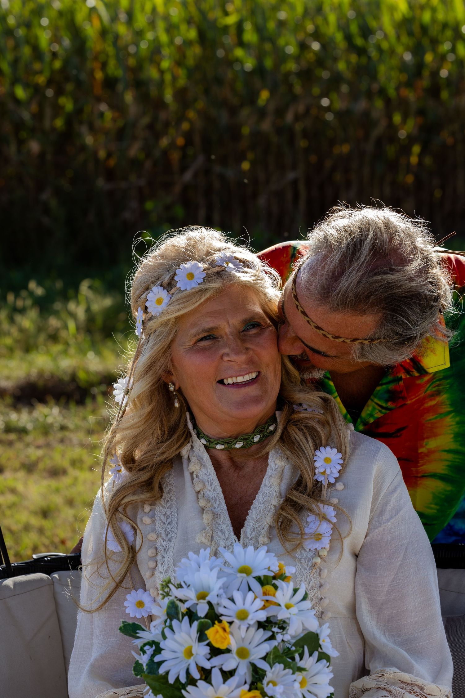 A couple shares a tender moment outdoors with a bouquet of daisies.