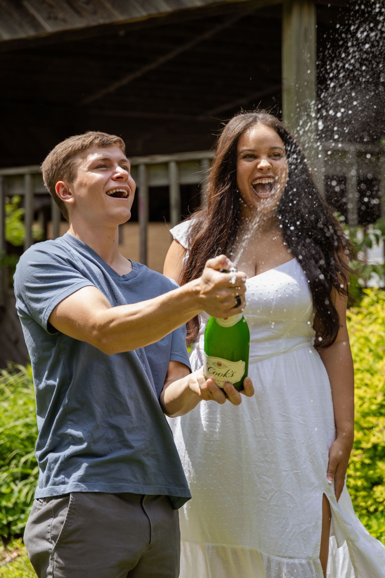 A celebratory moment with champagne spraying as a couple laughs together outdoors.