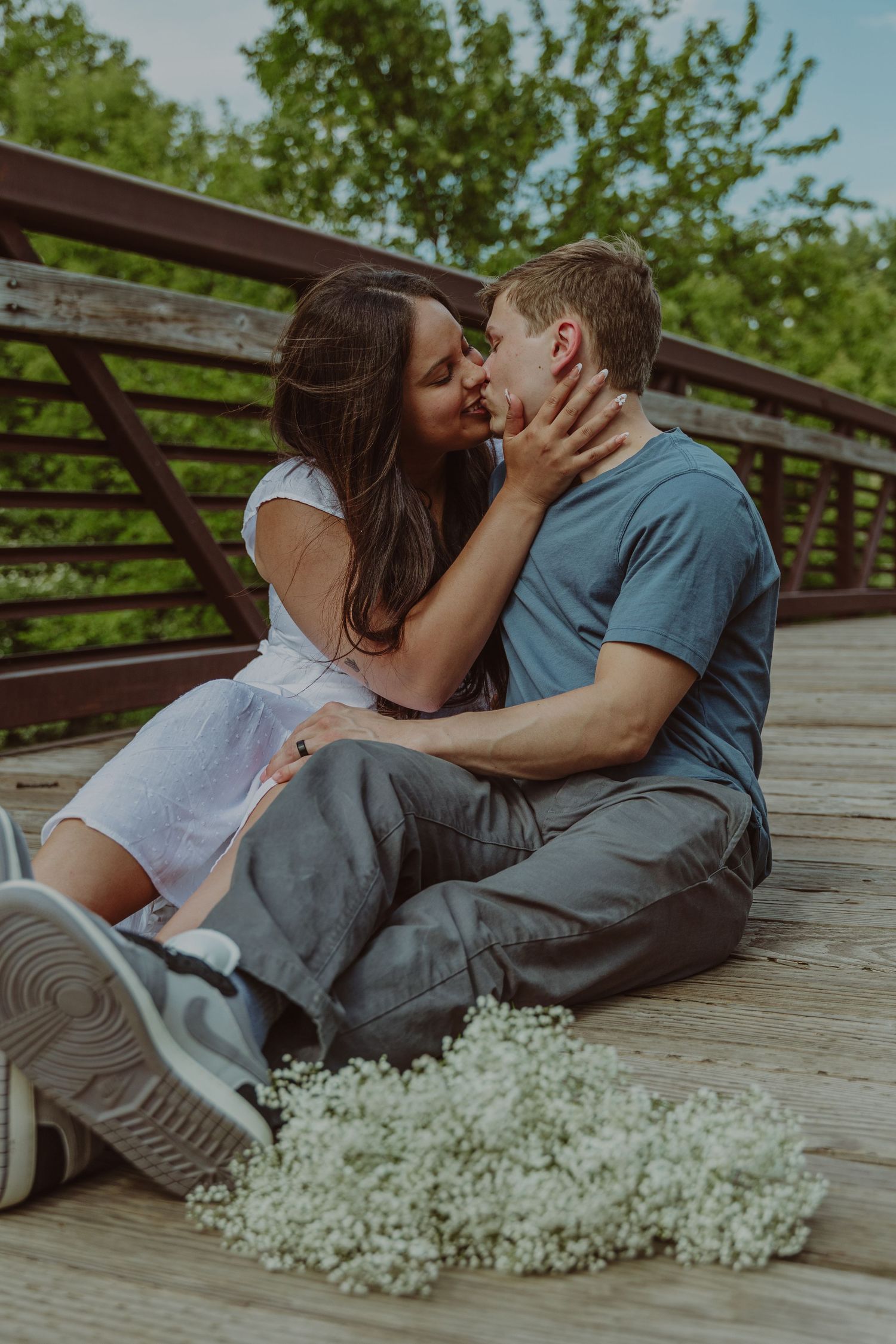 A romantic couple embraces on a wooden deck with baby's breath flowers nearby.
