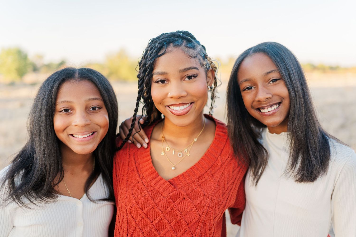 Three friends smile warmly while standing together outdoors during a golden hour photoshoot.
