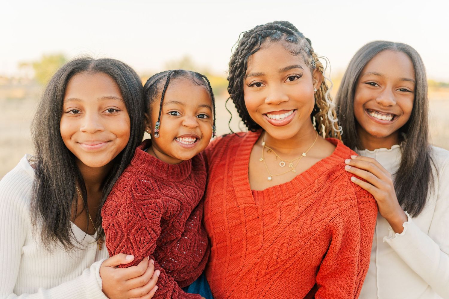 Four friends share joyful smiles while embracing during an outdoor photo session.