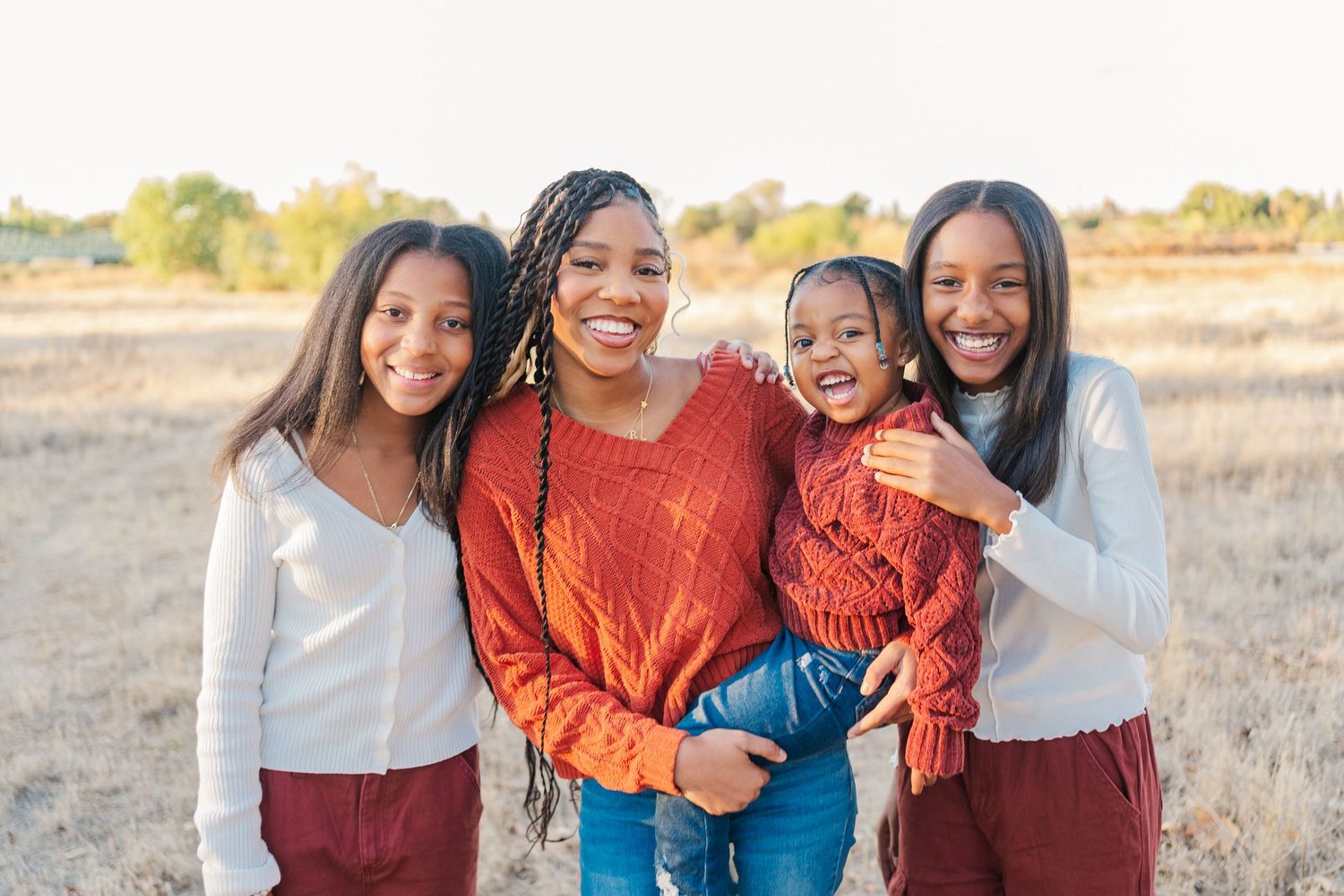 A cheerful group wearing coordinated outfits poses together in a field at sunset.