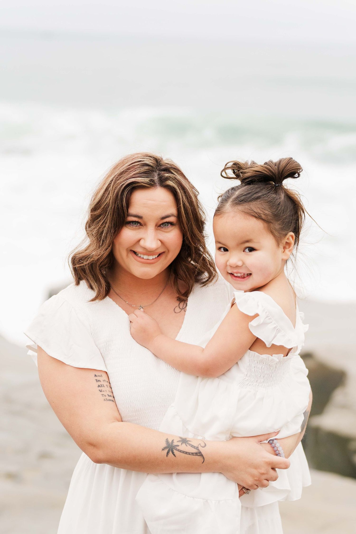 A tender beach portrait moment with matching white dresses against the ocean backdrop.