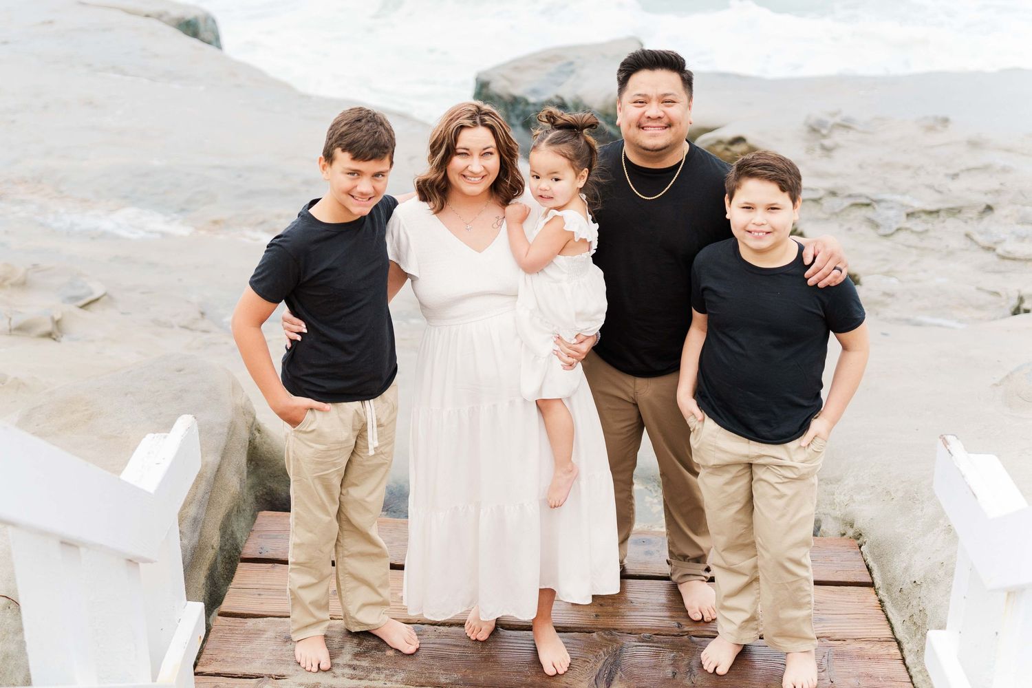 A family stands together on concrete steps near the ocean.
