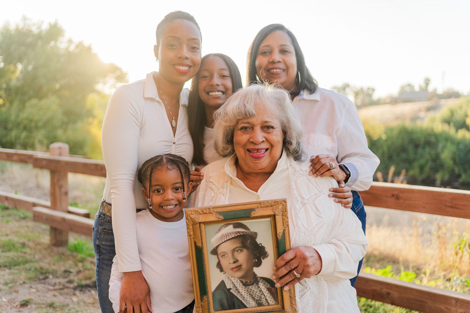 Family members gather outdoors holding a framed photograph during a memorial photoshoot.