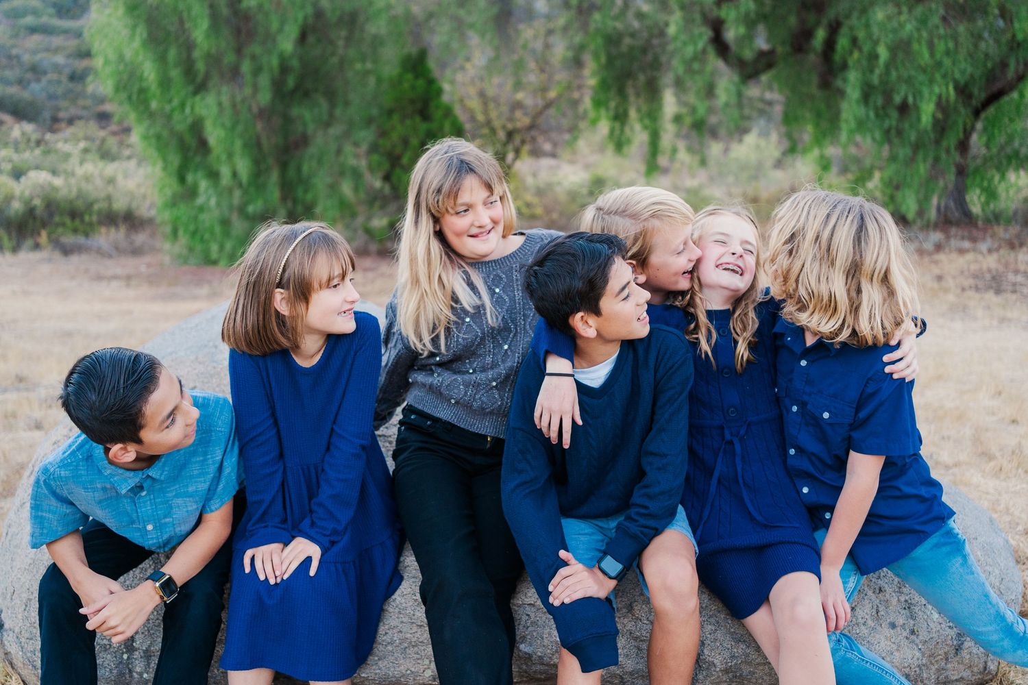 A group sits together outdoors sharing laughs against a natural backdrop.