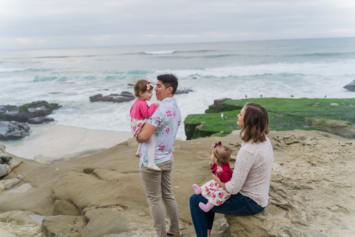 A family enjoys time together on rocky coastal cliffs overlooking the ocean.