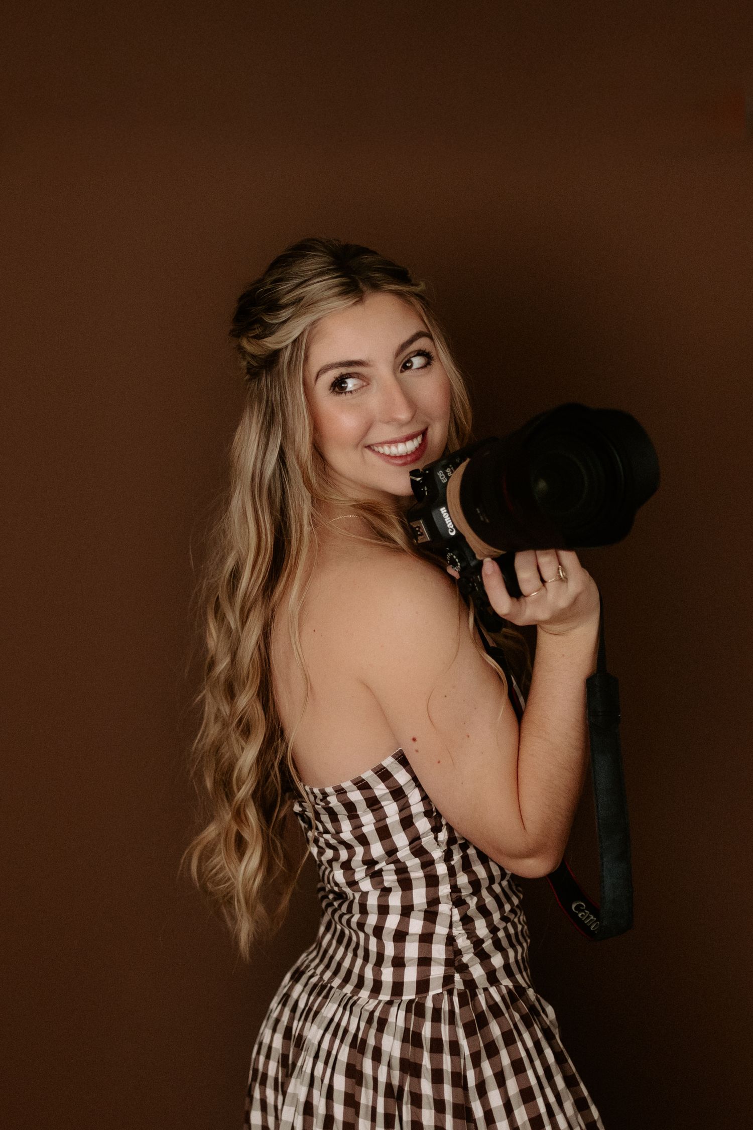 Photographer sitting cross-legged on white bedding holding professional camera with natural backdrop.