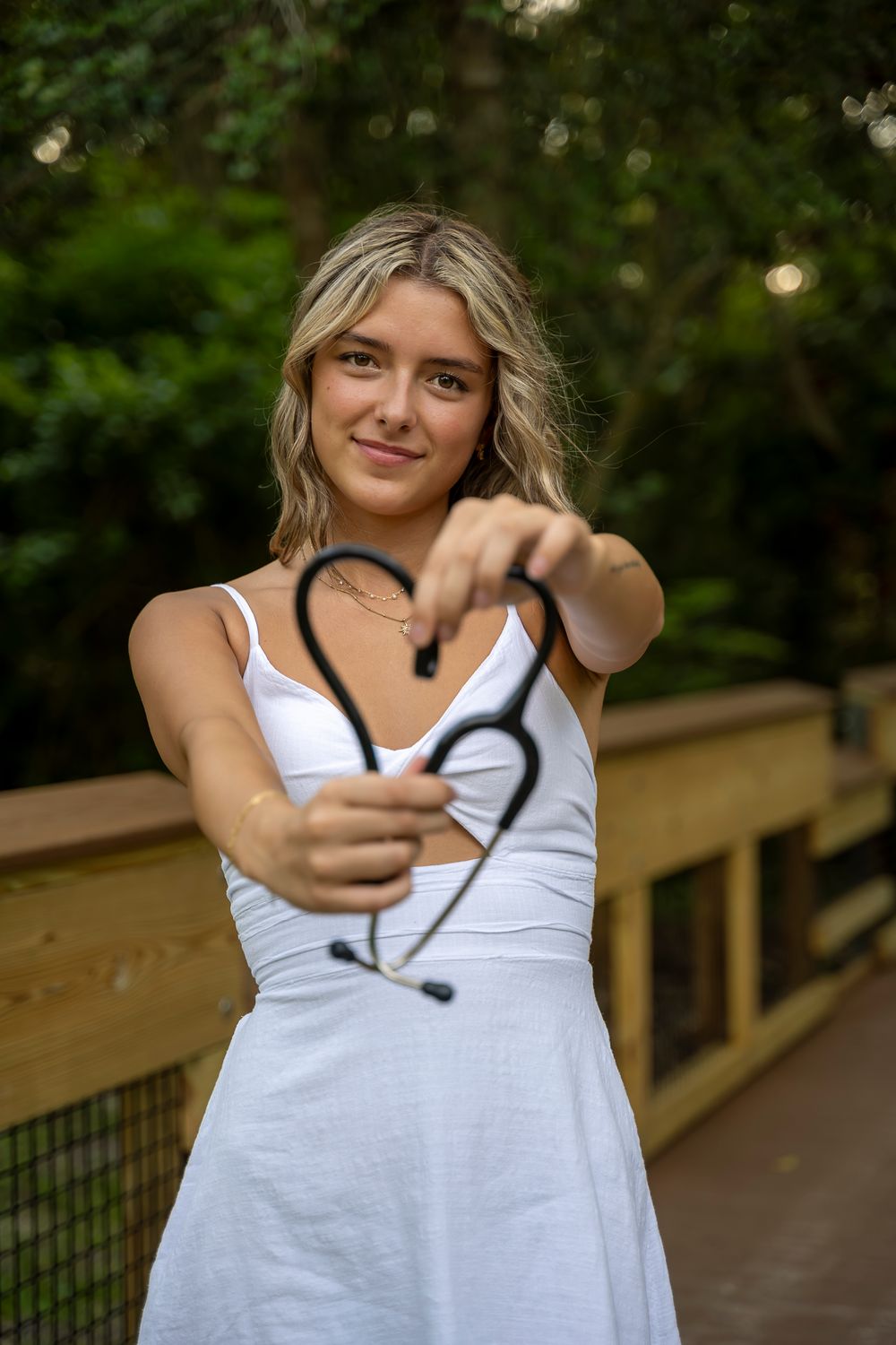 Person in white sleeveless top stands on wooden walkway in dappled sunlight.