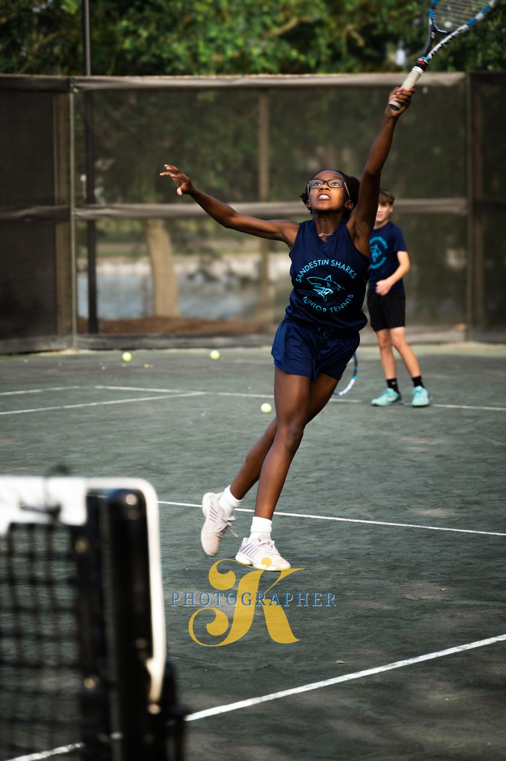 Tennis player in navy blue uniform jumps to serve the ball on outdoor court during competitive match.