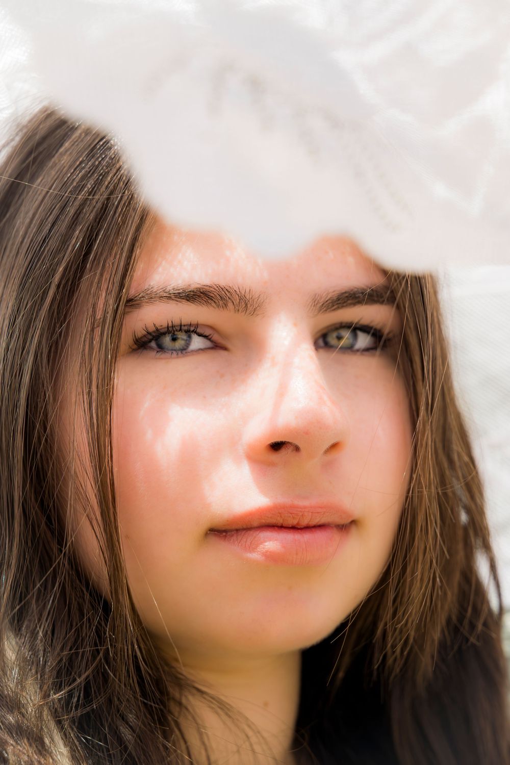 Close-up portrait of a young woman with green eyes and brown hair, partially covered by a white feather.