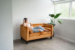 Pregnant woman relaxing on a tan leather loveseat in a minimalist room with plant decor.