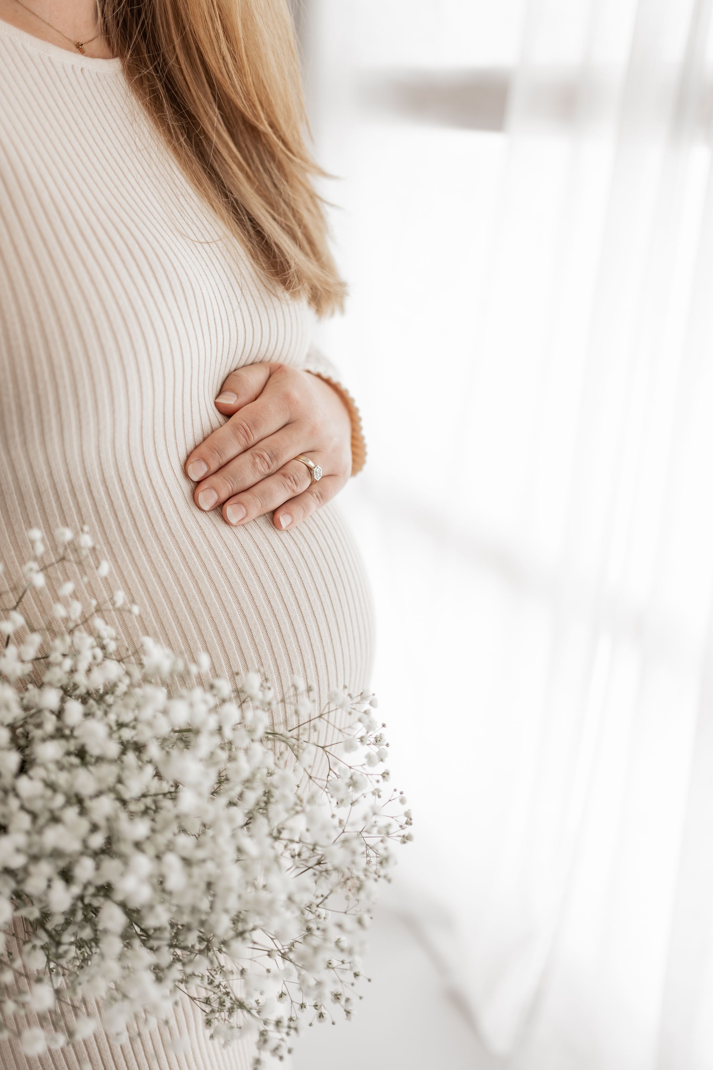 A person wearing a cozy white knit sweater holds delicate baby's breath flowers in soft natural lighting.