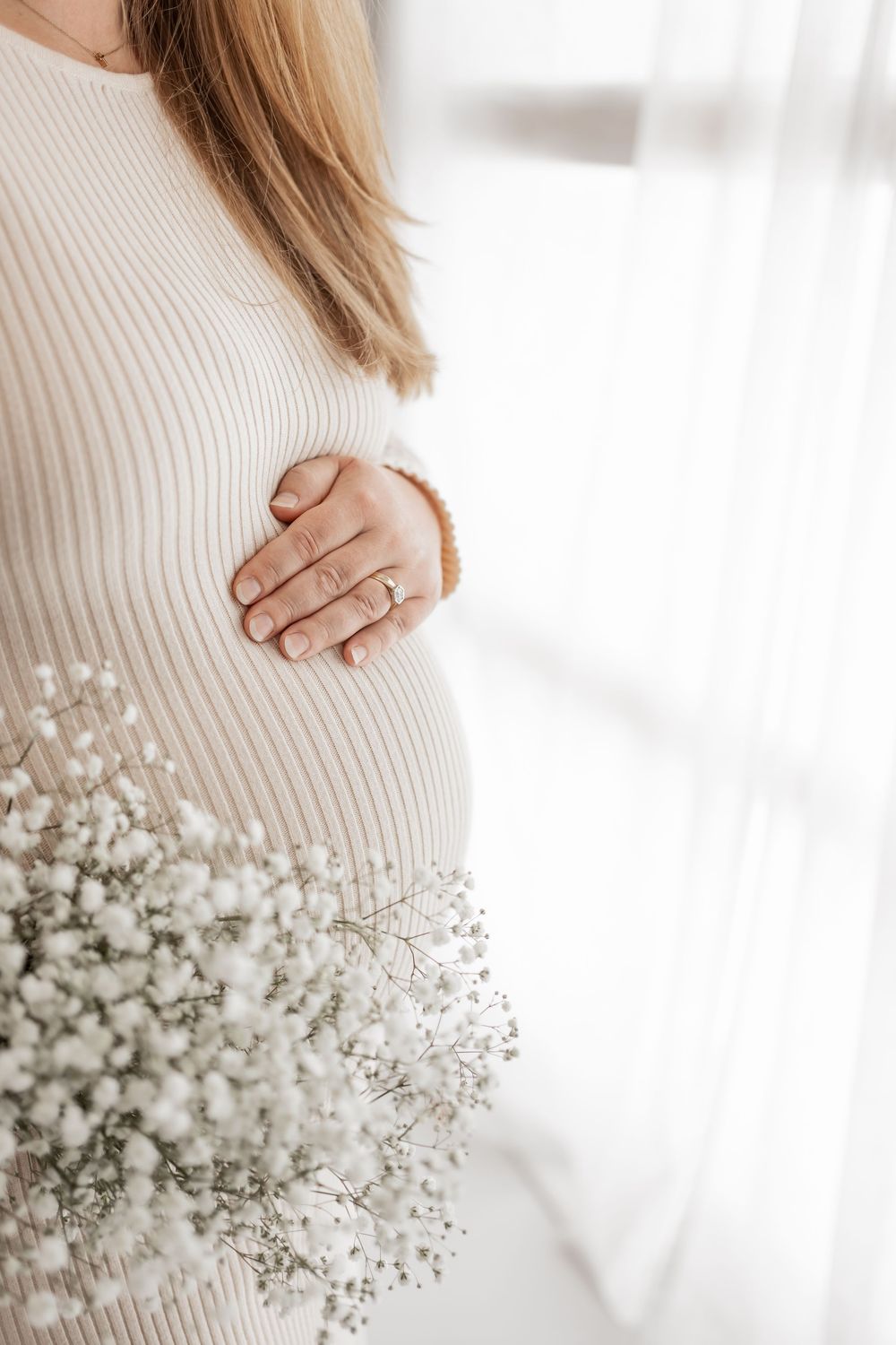A person wearing a cozy white knit sweater holds delicate baby's breath flowers in soft natural lighting.