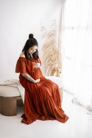 A series of artistic portraits showing a person in a flowing rust-colored dress seated against a minimalist white backdrop.