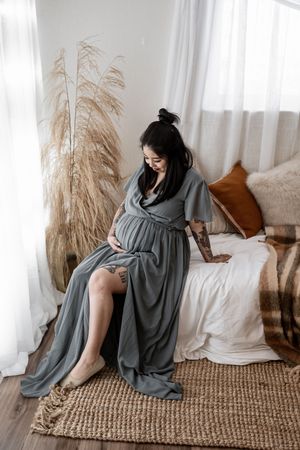 A person in a cozy gray blanket relaxes on a jute rug near dried pampas grass and white curtains.
