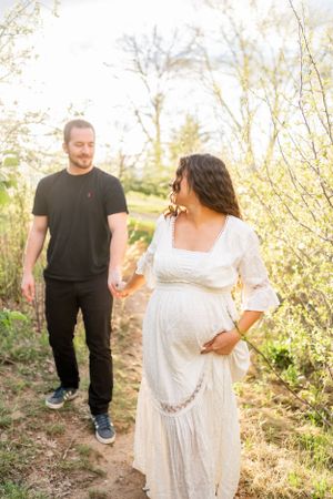 A couple walks together on a nature trail during golden hour with blossoming trees in the background.