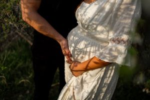 Close up of a flowing white maternity dress with sunlight casting dappled shadows.