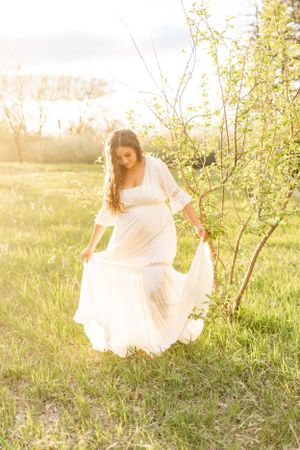 A flowing white dress twirls in a sunlit meadow surrounded by spring foliage.
