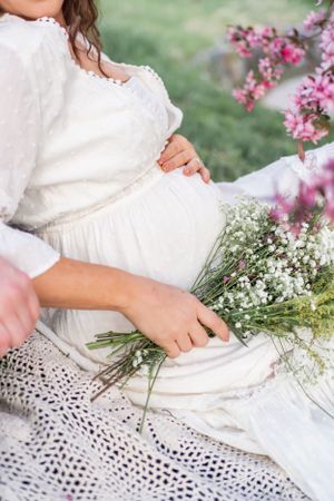 Close up of a white maternity dress with pink and white wildflowers arranged on a lace blanket.