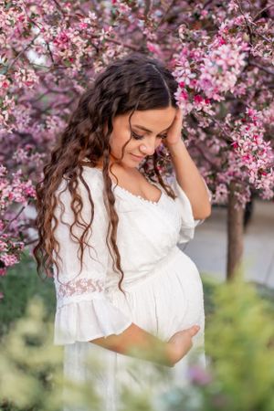 A dreamy spring maternity photo with blooming cherry blossoms in the background.