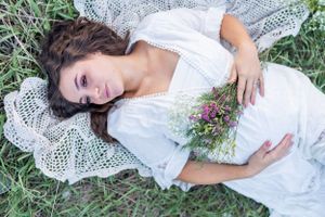 A maternity photo shoot on white lace with delicate flowers scattered around.