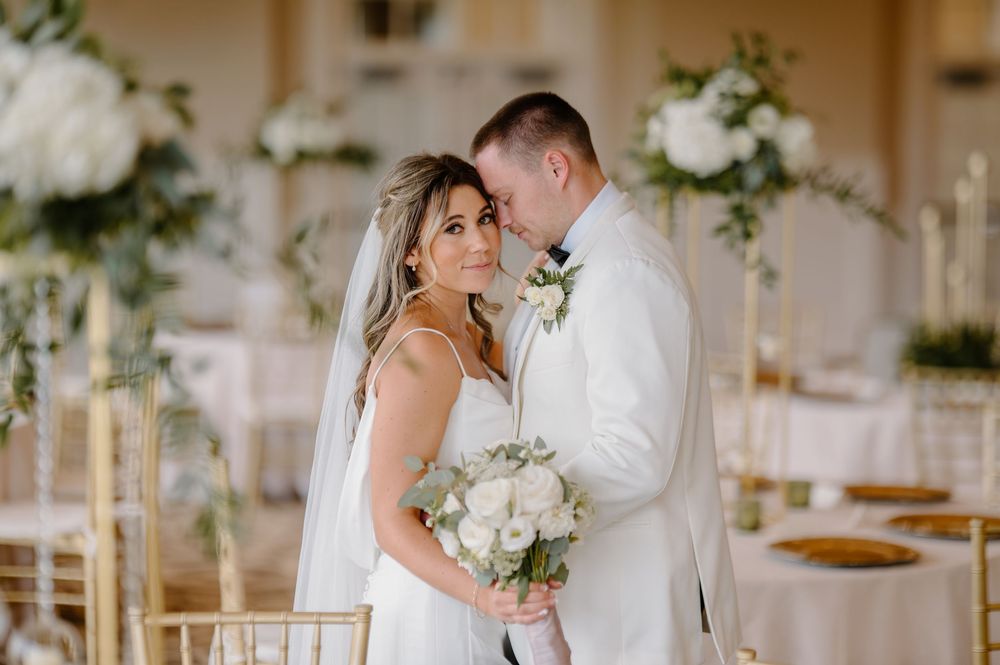 Elegant white floral wedding ceremony arch with drapery stands in a bright, sun-filled reception venue.
