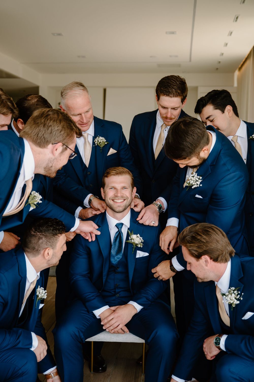 Five candid photos show groomsmen in navy suits sharing heartfelt laughter during a wedding celebration.