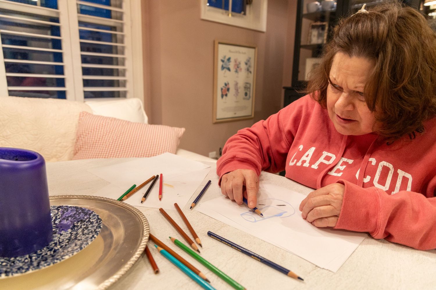 Elizabeth, a woman in her 60s with short brown hair, frowns while trying to draw a picture to depict her vision