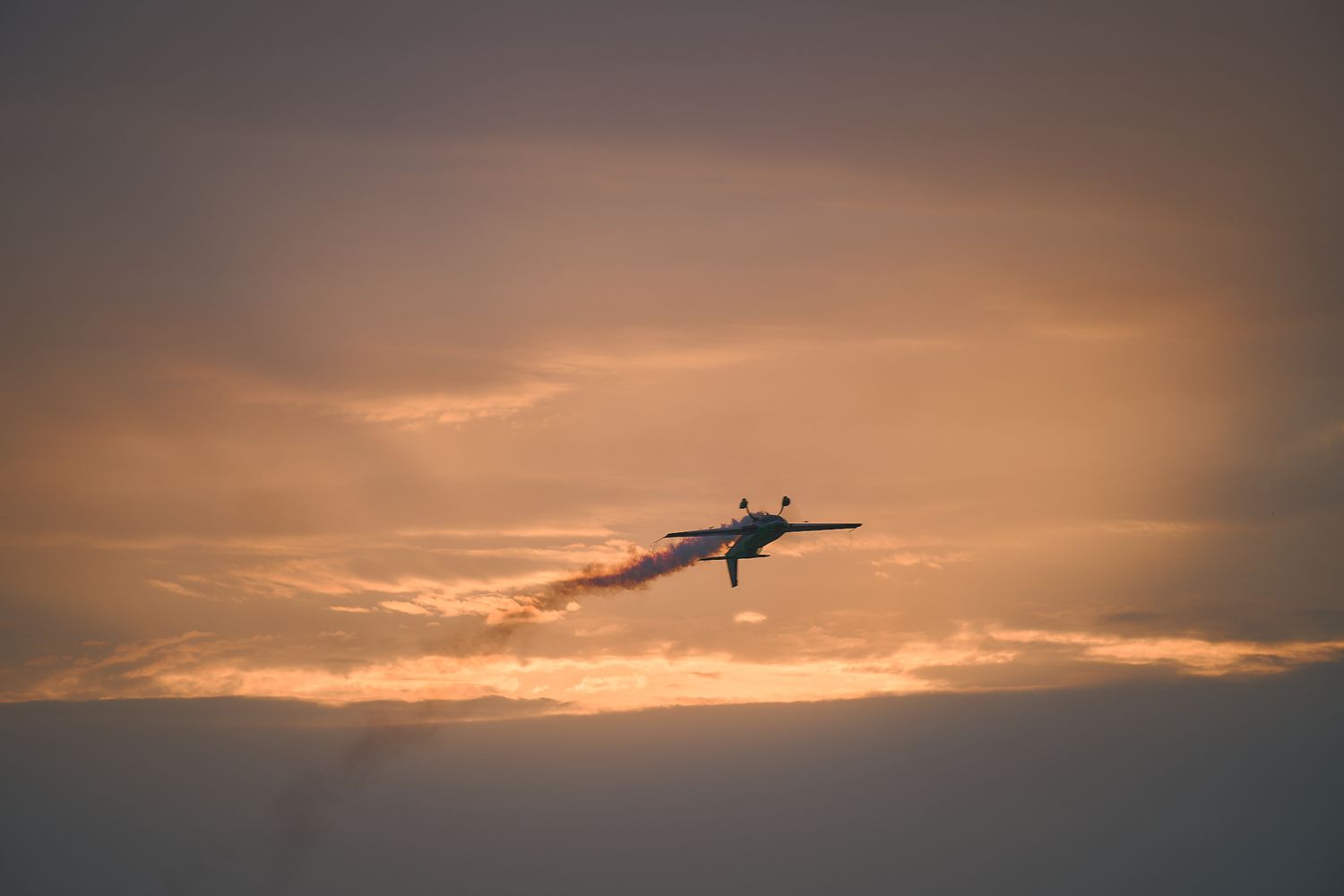 Silhouette of a military jet against an orange sunset sky with dramatic clouds.