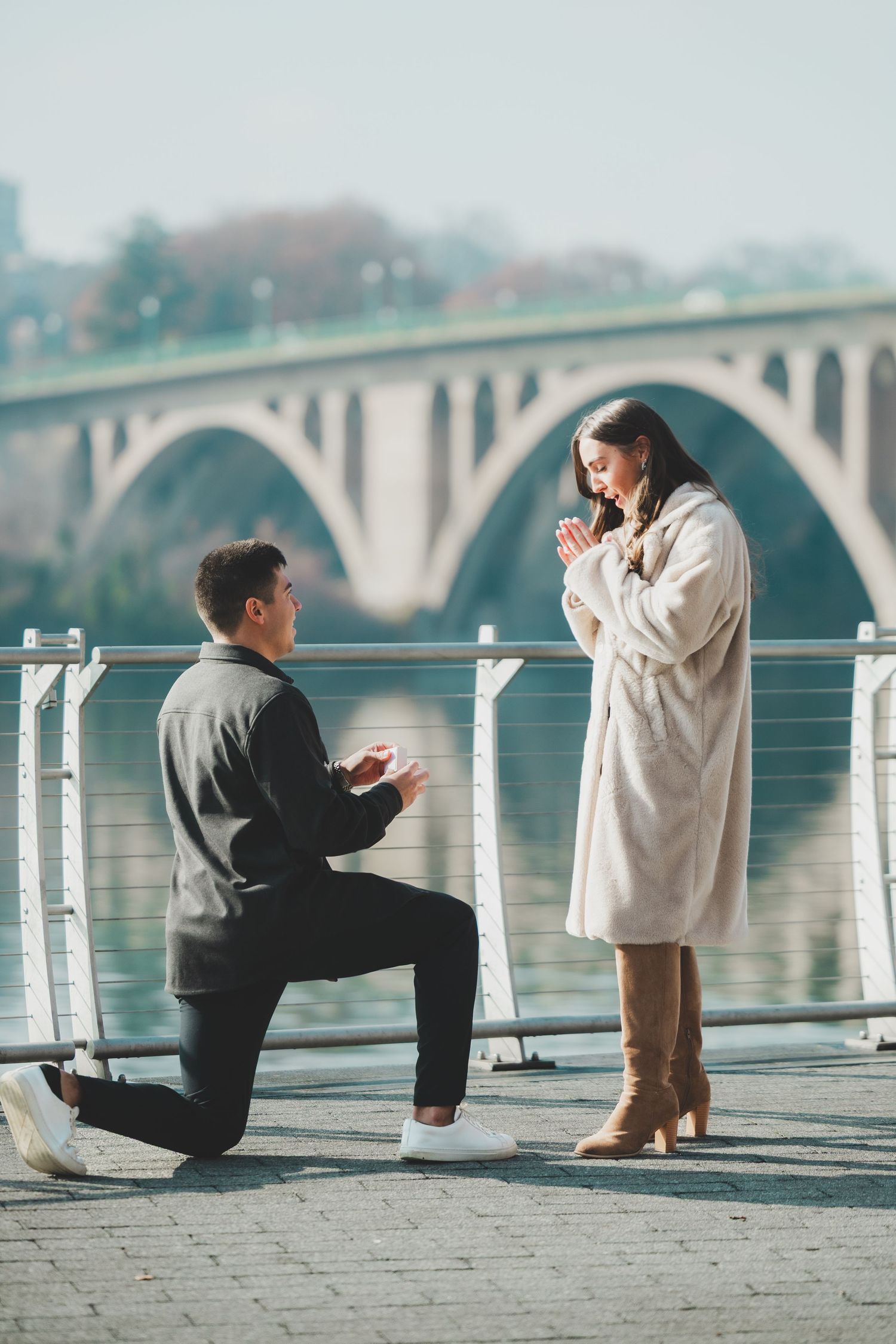 A romantic marriage proposal on a waterfront promenade in Georgetown Washington DC with an arched bridge in the background.