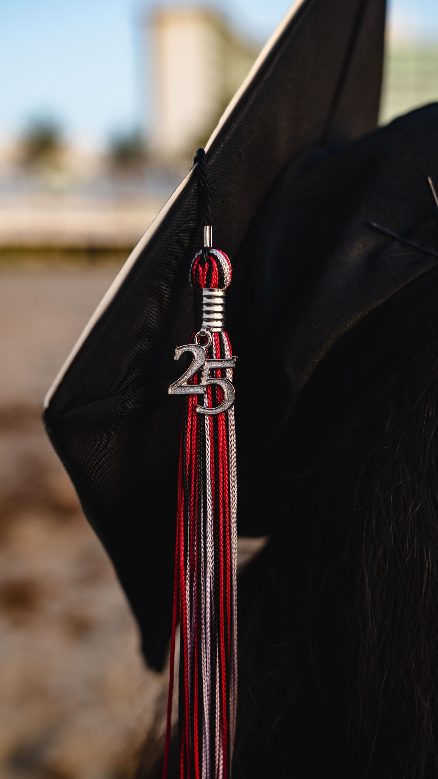 Red and white graduation tassels hanging from a black graduation cap captured in detail.
