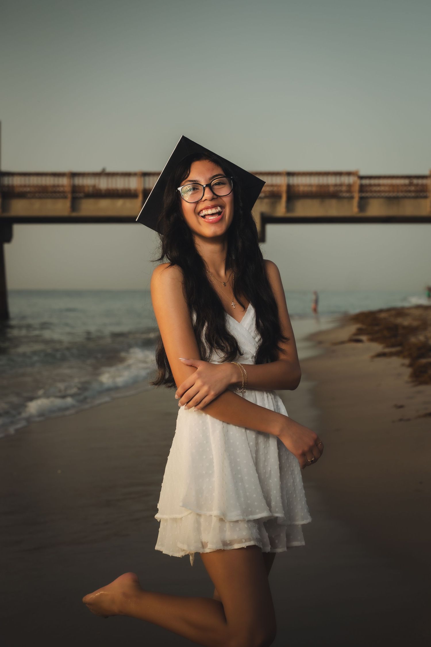 A woman in a white dress poses on a beach at sunset, creating a serene and joyful summer portrait.
