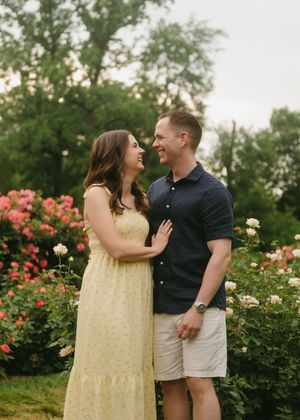 Couple laughing together in a rose garden, woman in yellow dress and man in navy shirt.