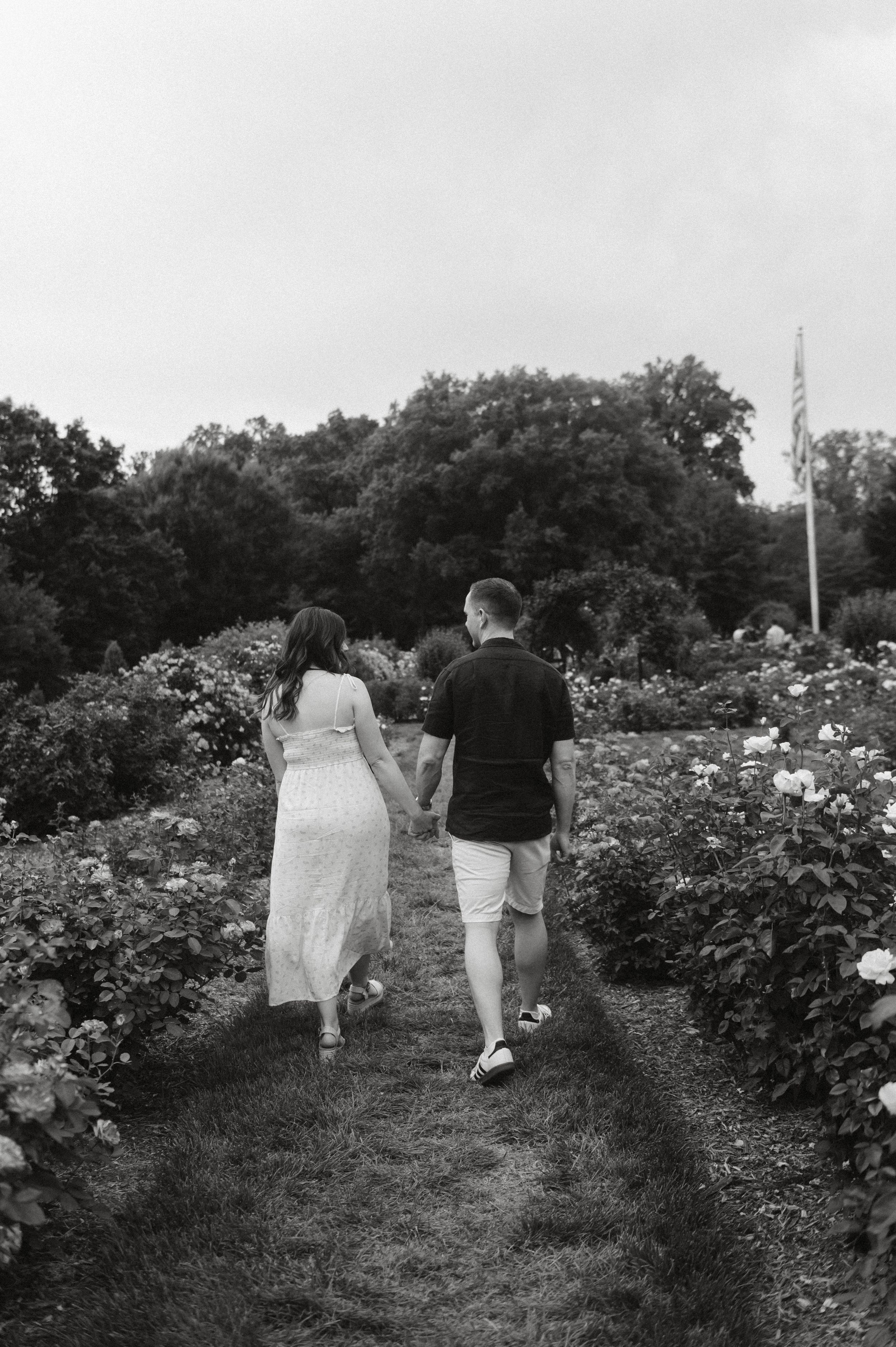 Couple walking hand in hand through a blooming garden path in black and white photo.