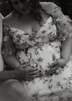 Black and white maternity photo of couple cradling pregnant belly in floral dress.