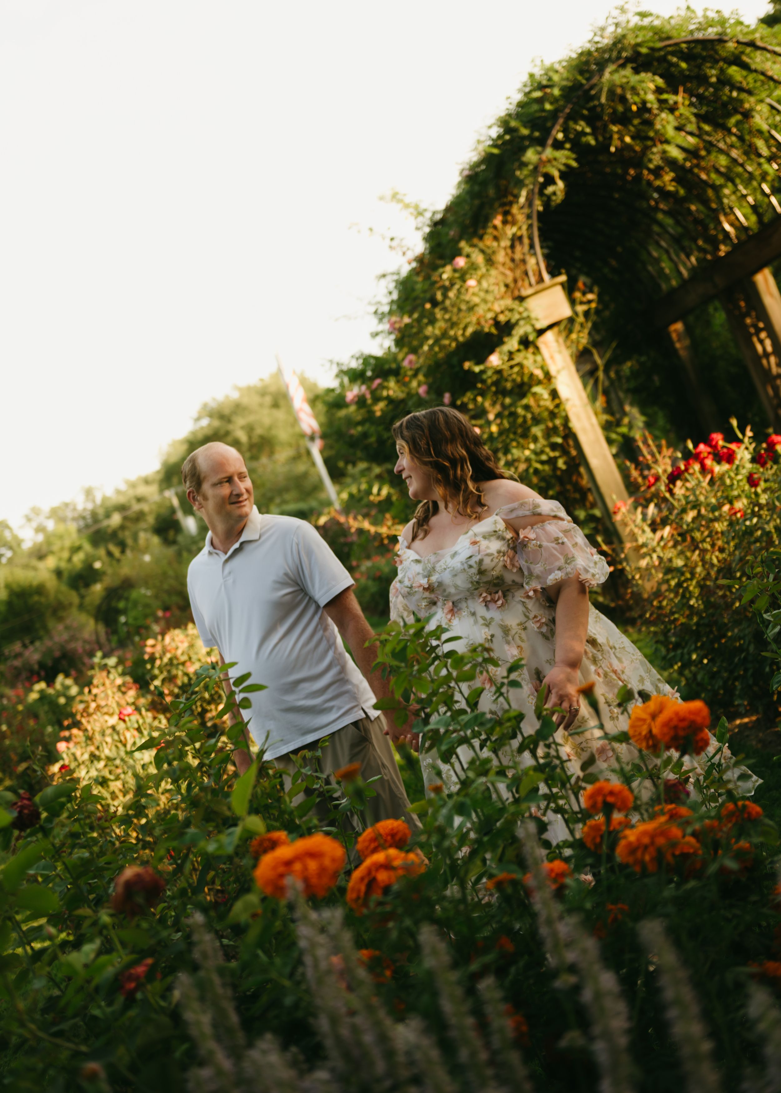 Couple walking through a lush garden with orange marigolds and greenery in warm golden hour light.