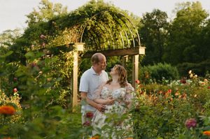 Couple shares a romantic moment under a floral garden archway surrounded by colorful blooms in golden hour light.