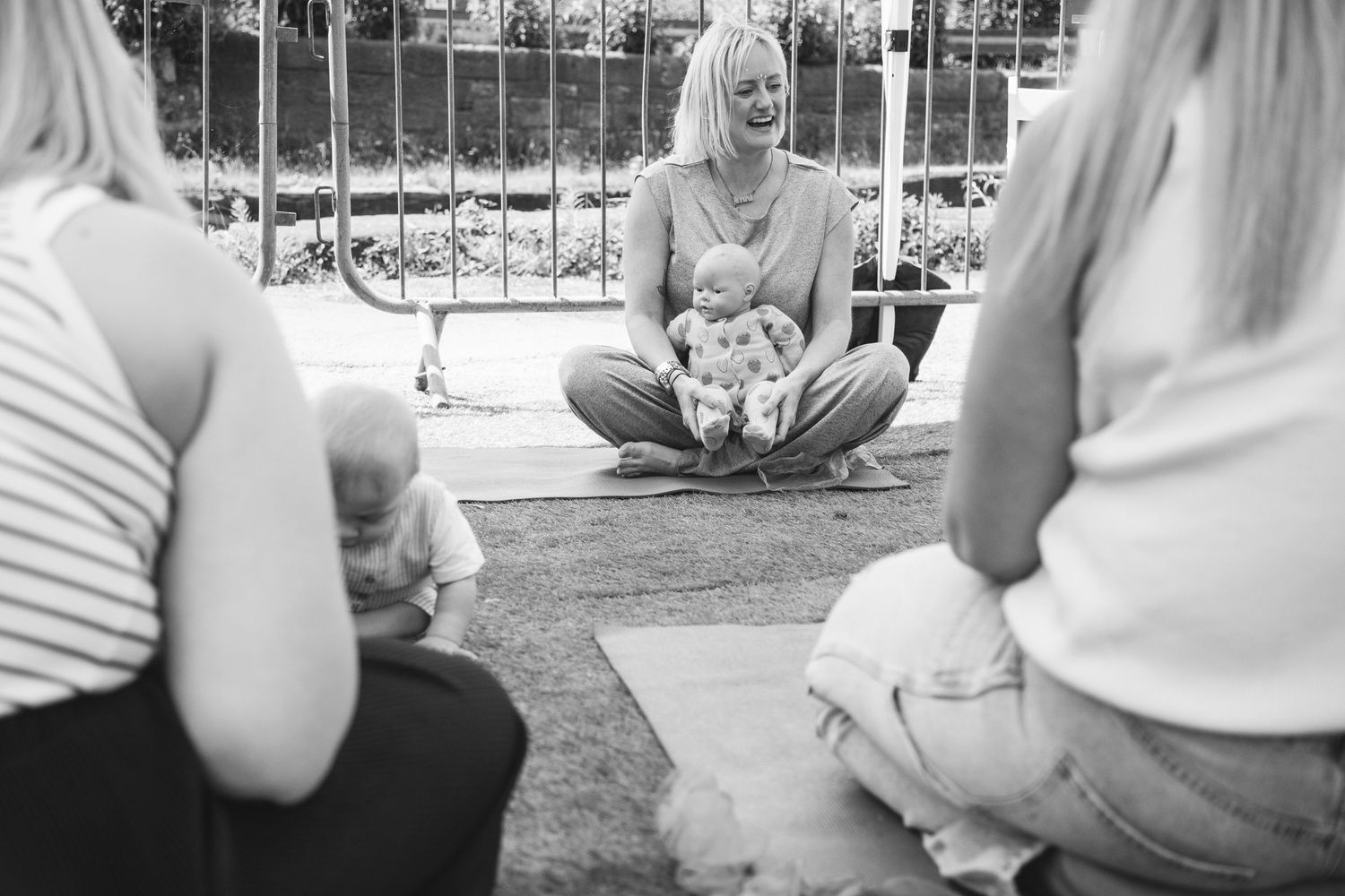 Black and white image of a group fitness class seated in a circle on exercise mats outdoors.