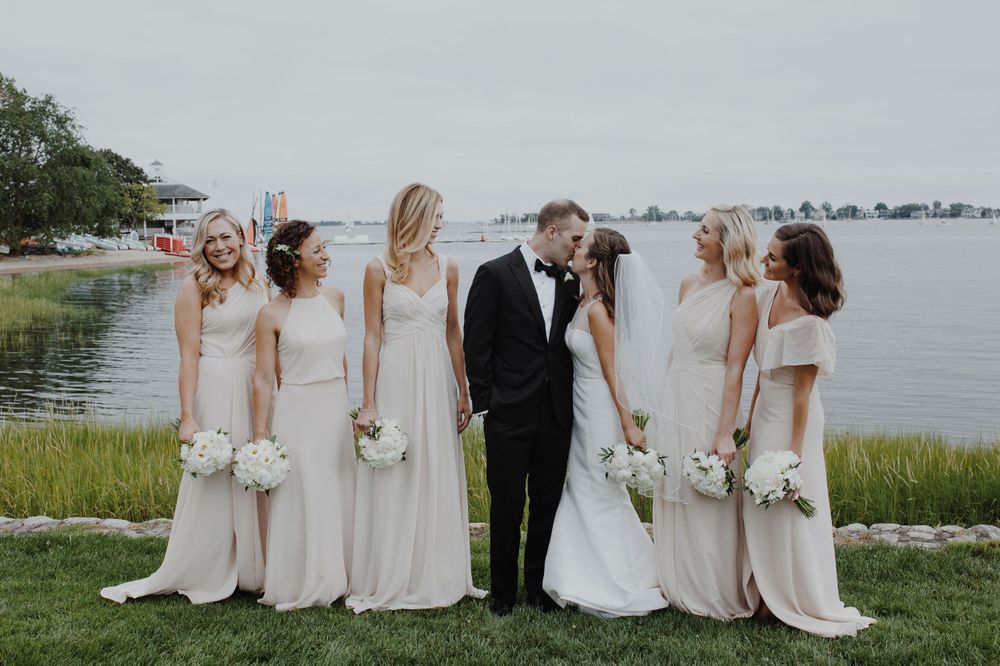 Wedding party poses by the waterfront with bridesmaids in matching light gowns.
