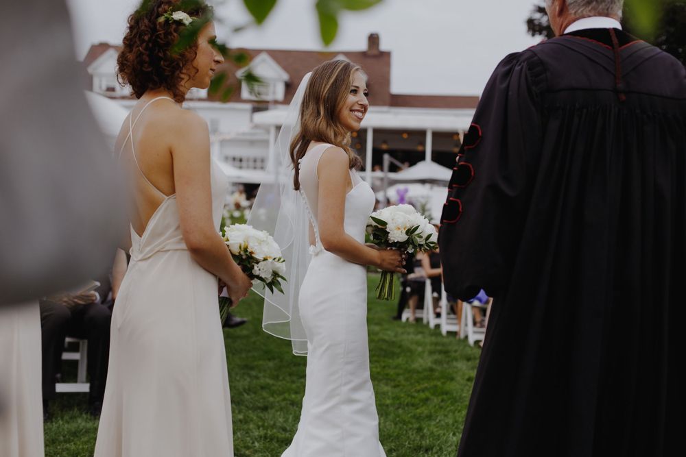 Wedding party members in elegant white dresses stand during outdoor ceremony.