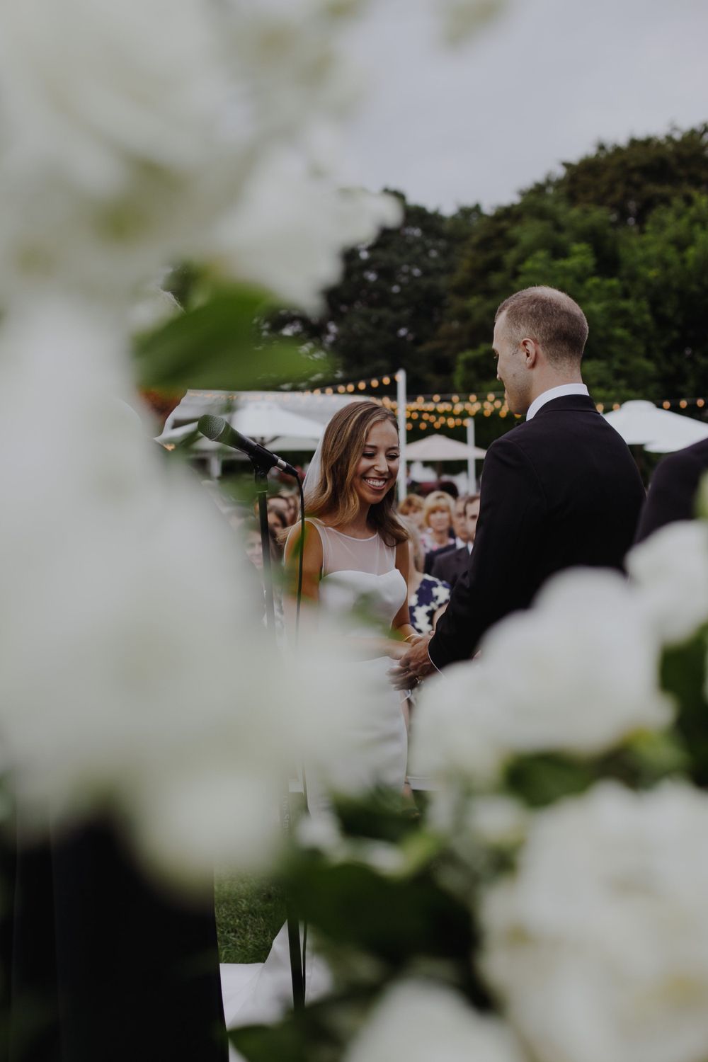 A romantic outdoor wedding ceremony moment captured through white flowers in the foreground.