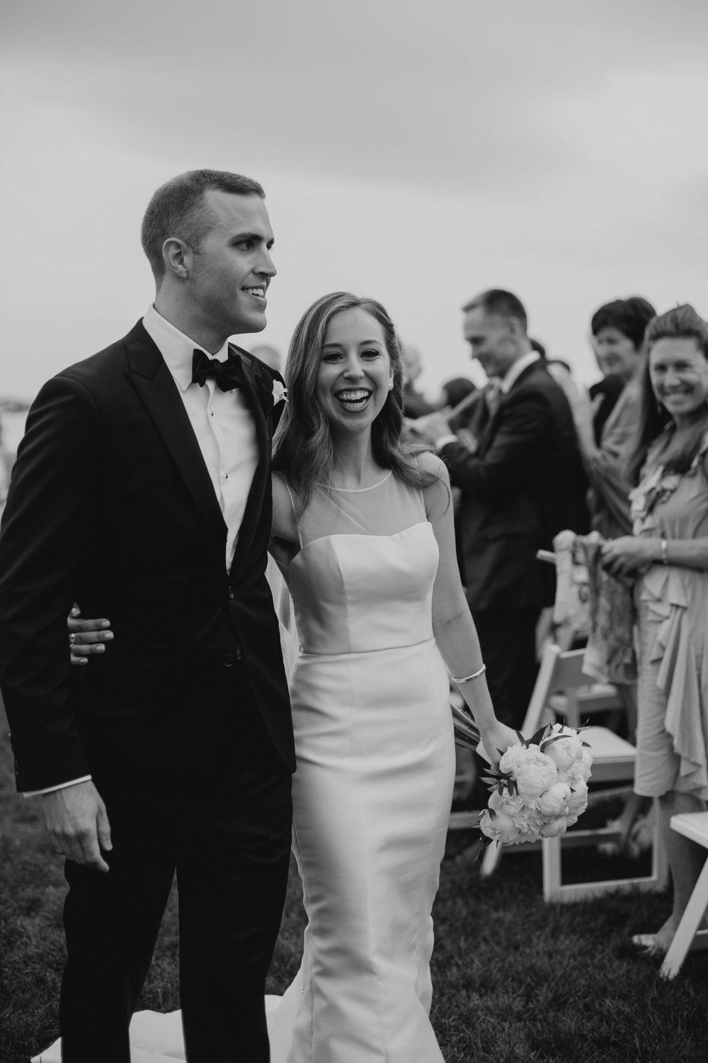 Joyful wedding recessional moment captured in black and white by the water.