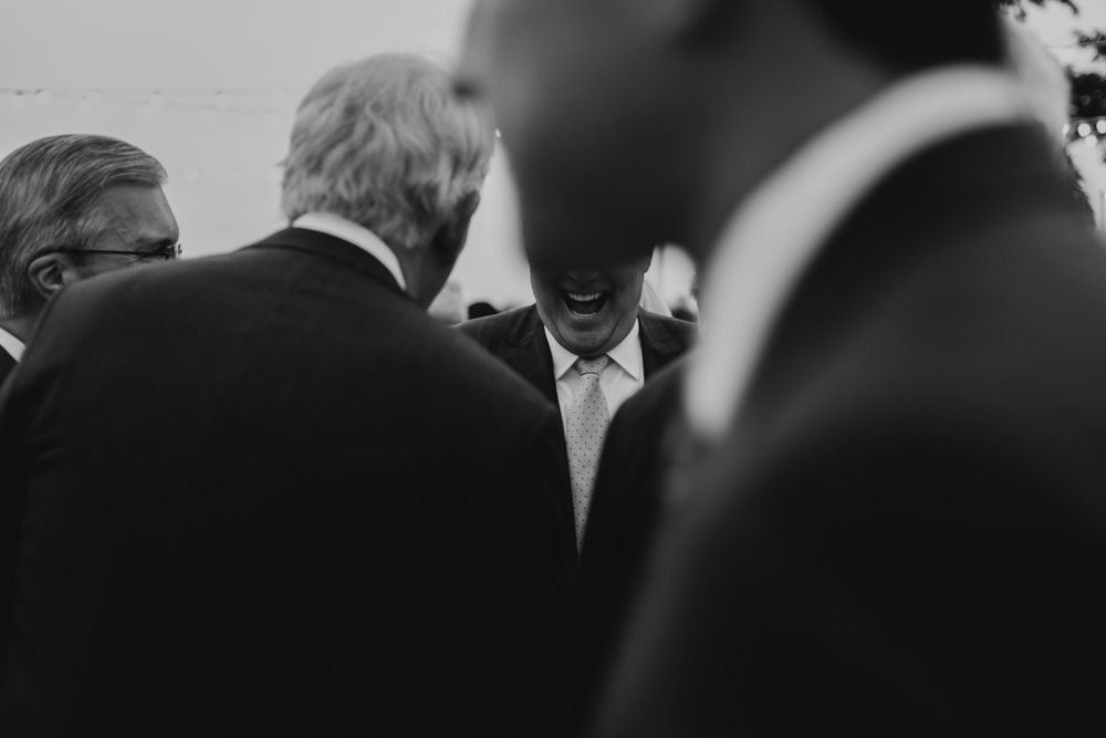 Formal gathering showing guests in dark suits engaged in conversation.