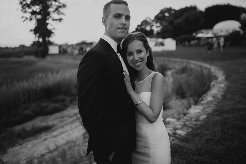 Black and white wedding portrait of couple posing along curved path at dusk.