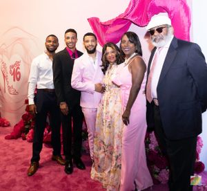 Group photo at formal event with pink backdrop featuring people in elegant attire against floral decorations.