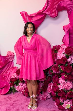Woman wearing flowing pink dress with bell sleeves stands against vibrant pink floral backdrop.