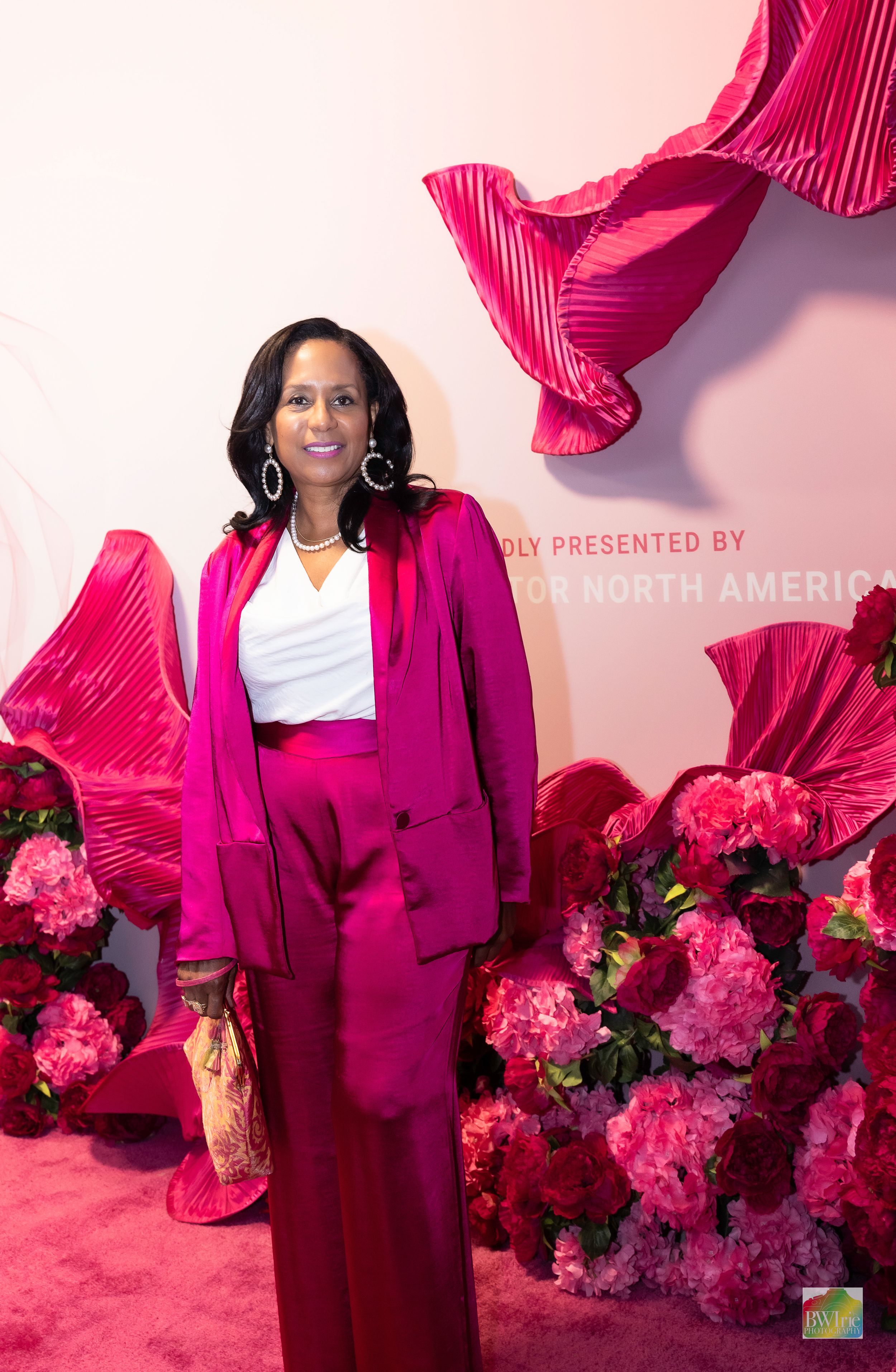 A person wearing a vibrant hot pink suit poses in front of a floral wall display.