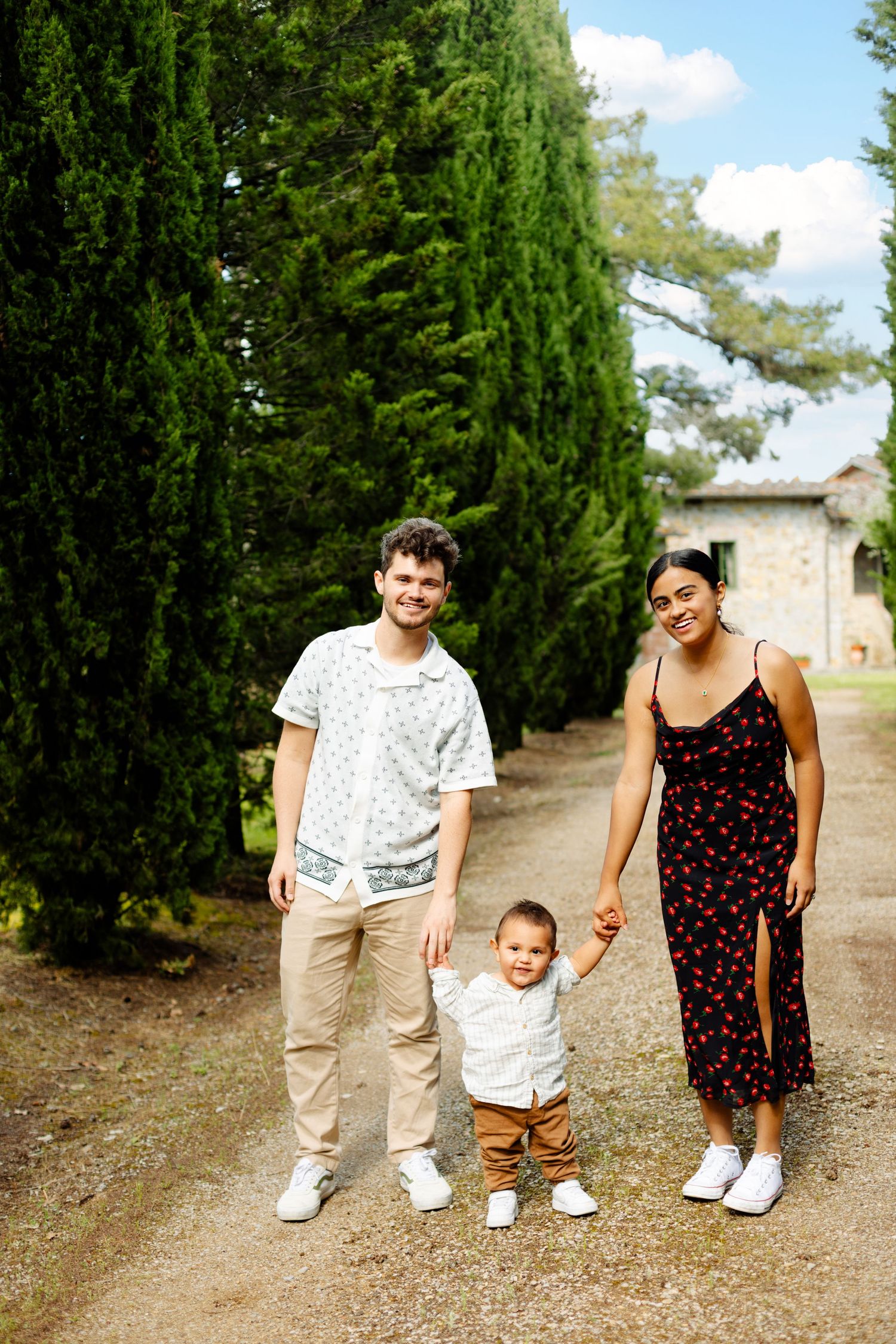 Family standing together on a path lined with tall cypress trees on a sunny day.