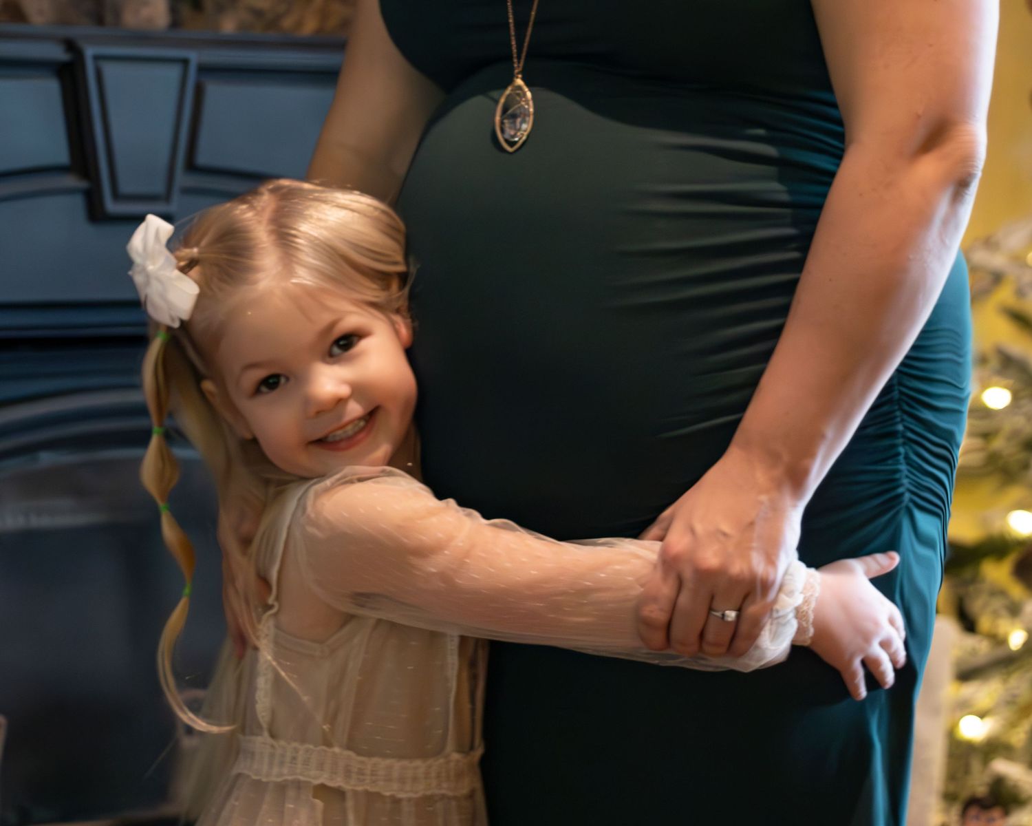 A young girl hugs her pregnant mother with her face against the belly. The mother's face is out of frame